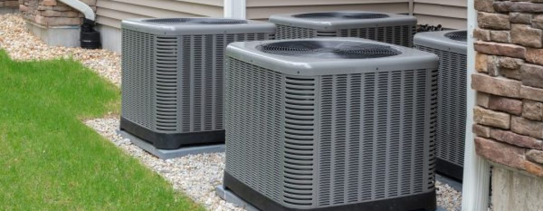 four gray ac units side by side and front to back behind a residental home and set on a stone foundation